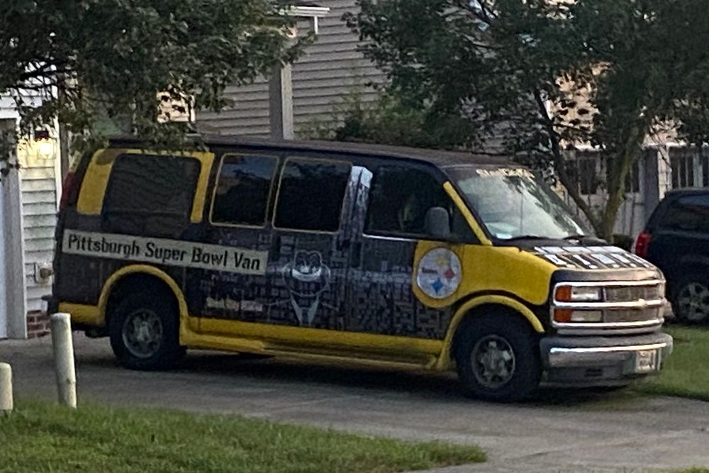A cargo van painted gold and grey with “Pittsburgh Super Bowl Van” written on the side, and the team logo circle with the “Steelers” and yellow, red, and blue stars. 
