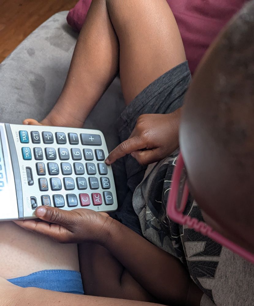 Little boy sitting next to his mother on a couch playing with a calculator 