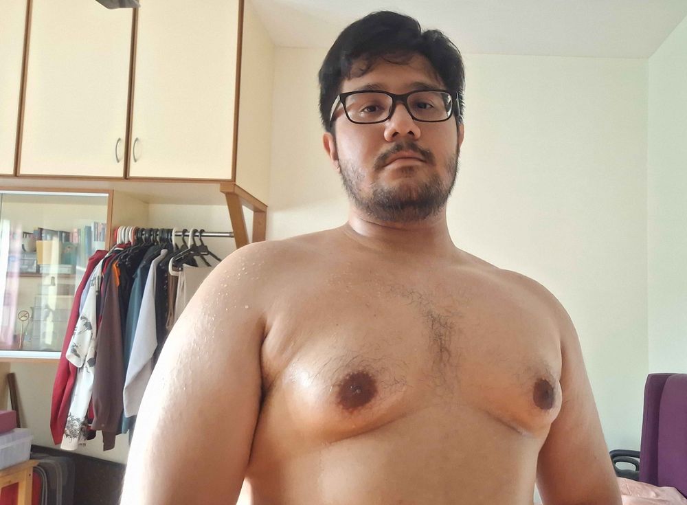 A picture of me shirtless, showing my head and the top half of my torso. I'm sweating and my tits are fat and muscular.