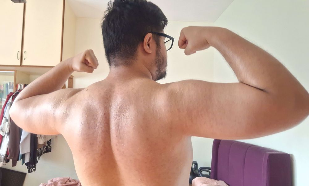 This time I am facing away from the camera, but still flexing. My back is broad and sweaty. Not as well defined, but the sunlight shows the subtle musculature of my back.