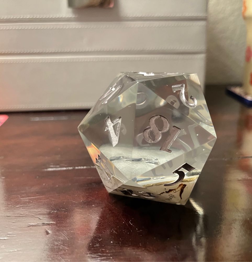 a translucent 20 sided die with silver numberings on the side, and a broken silver sword inside the die itself