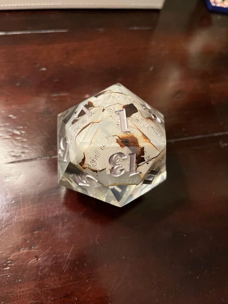 an image of a translucent 20 sided die, with burnt pieces of paper with elven text on them
