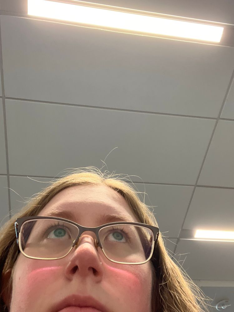 image of a woman with glasses looking off to the side. she’s peeking out of the corner but looks exhausted