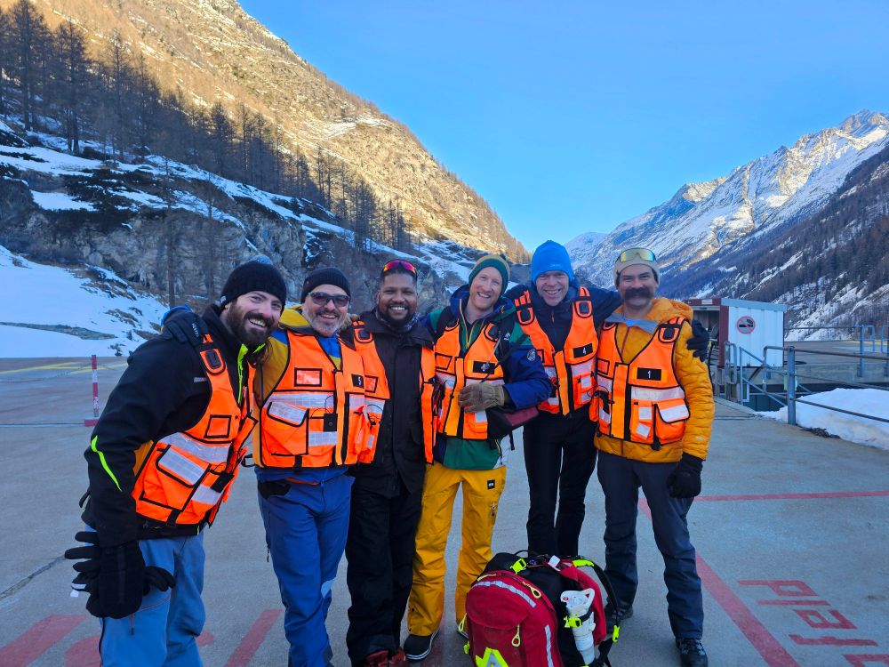 Team orange together on the Air Zermatt helipad, scenic mountain vista behind
