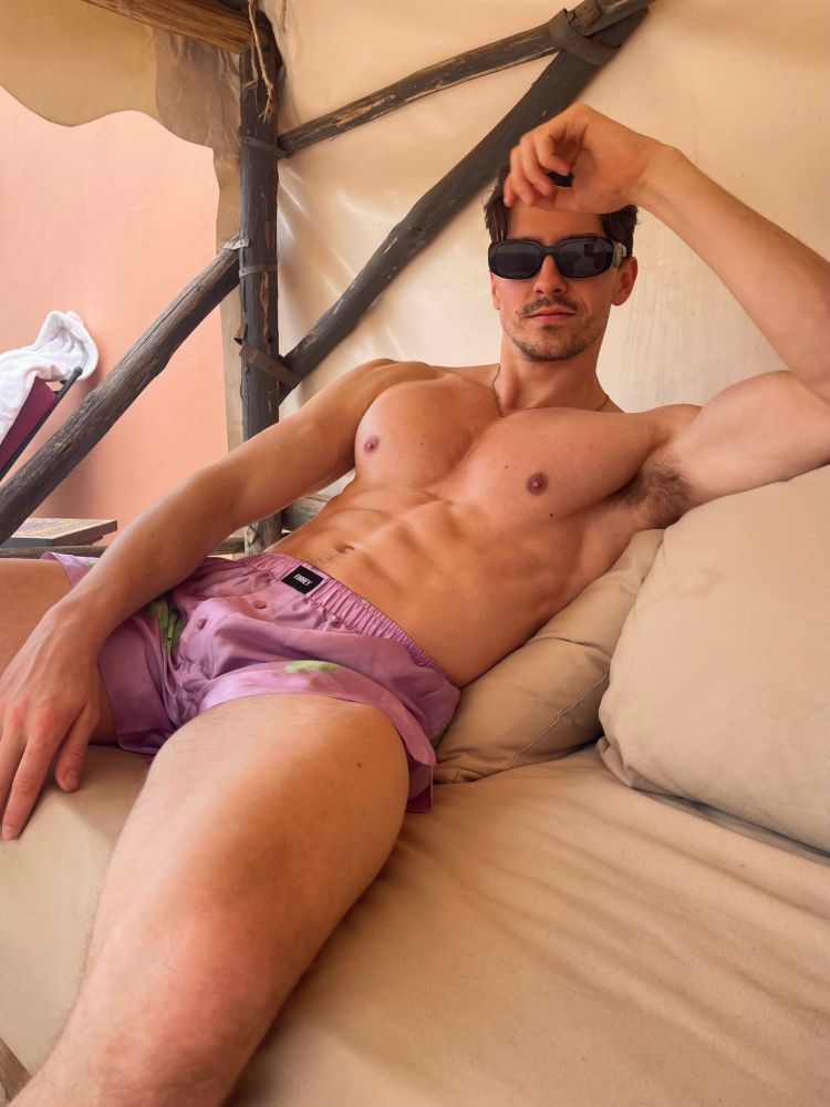 Un jeune homme imberbe et musclé est sur un sofá extérieur. Il porte un caleçon en matière toute douce mauve. Il a des lunettes de soleil et des aisselles poilues.
Visiblement il a des gros biceps en plus d'avoir des gros pecs et d'avoir aussi des jambes musclées.

