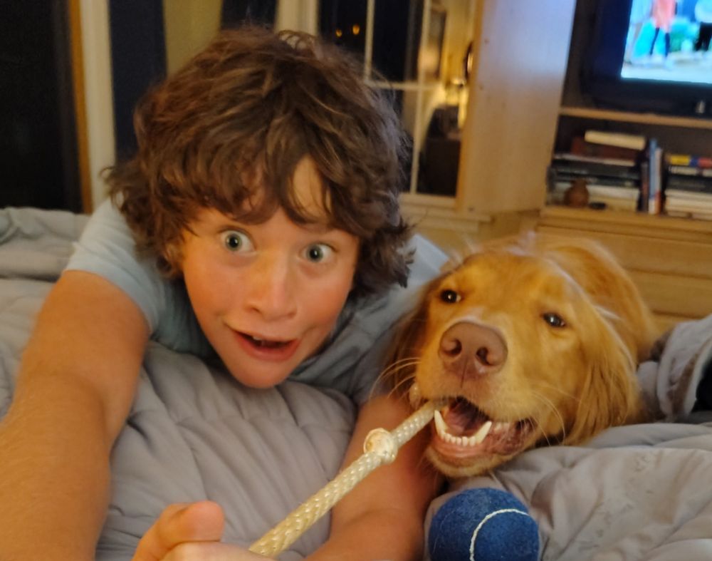 Boy and dog tugging on a rope with the boy making an excited golden retriever style excited expression.