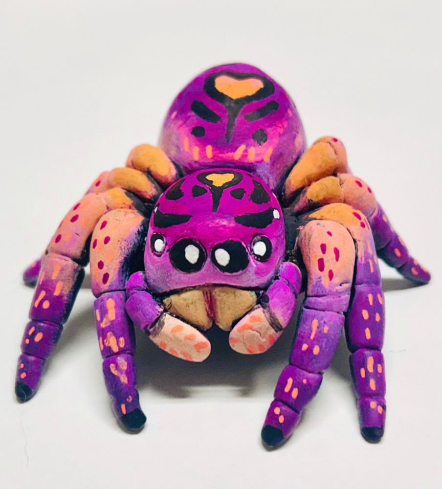 An orange and pinkish purple lesbian flag jumping spider made out of clay 