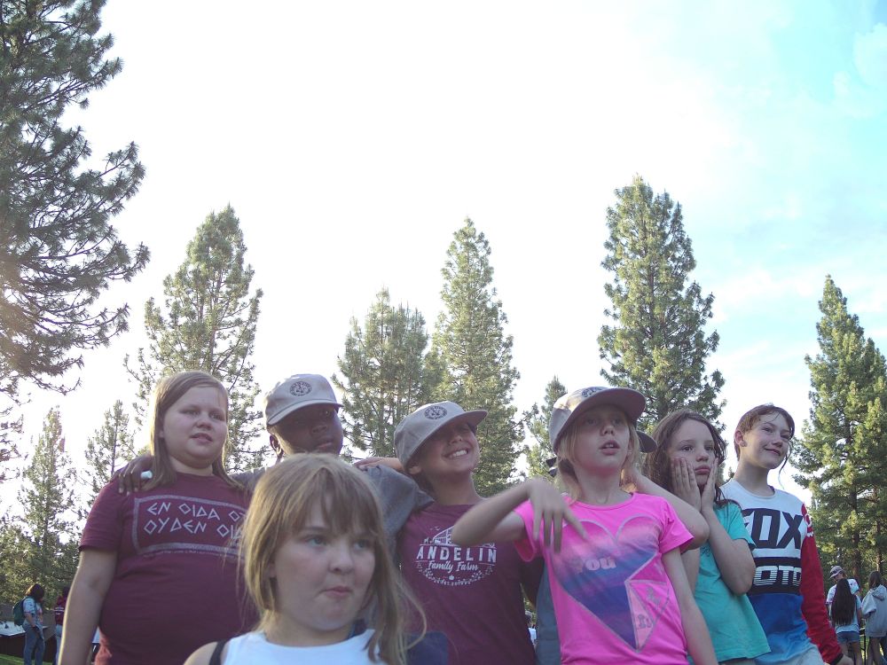 Seven campers stand in front of tall trees.