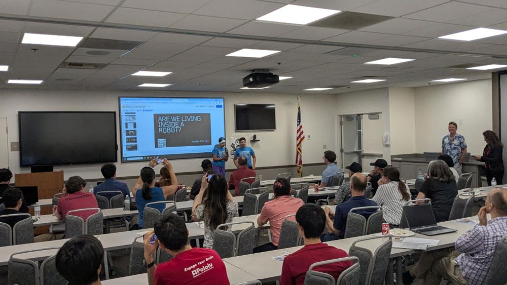 Students speak in a conference room to a group of adults seated at tables.