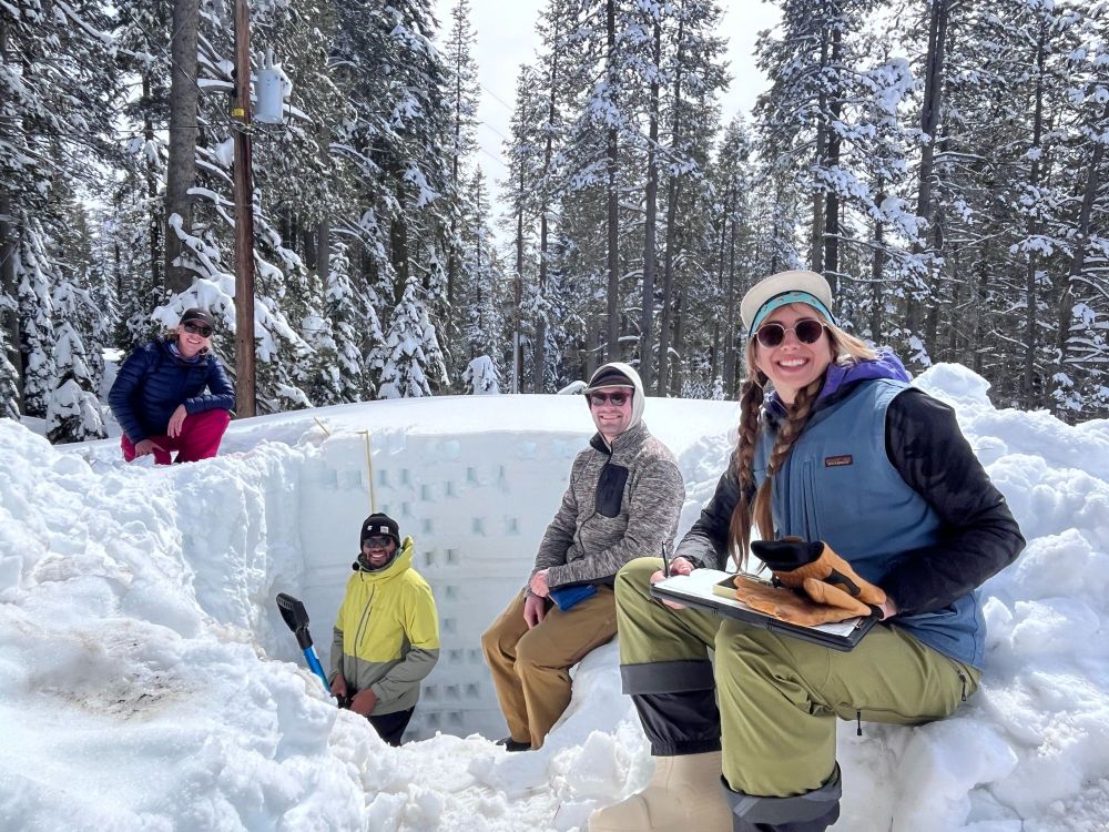 Researchers smiling and posing around a snow pit. 