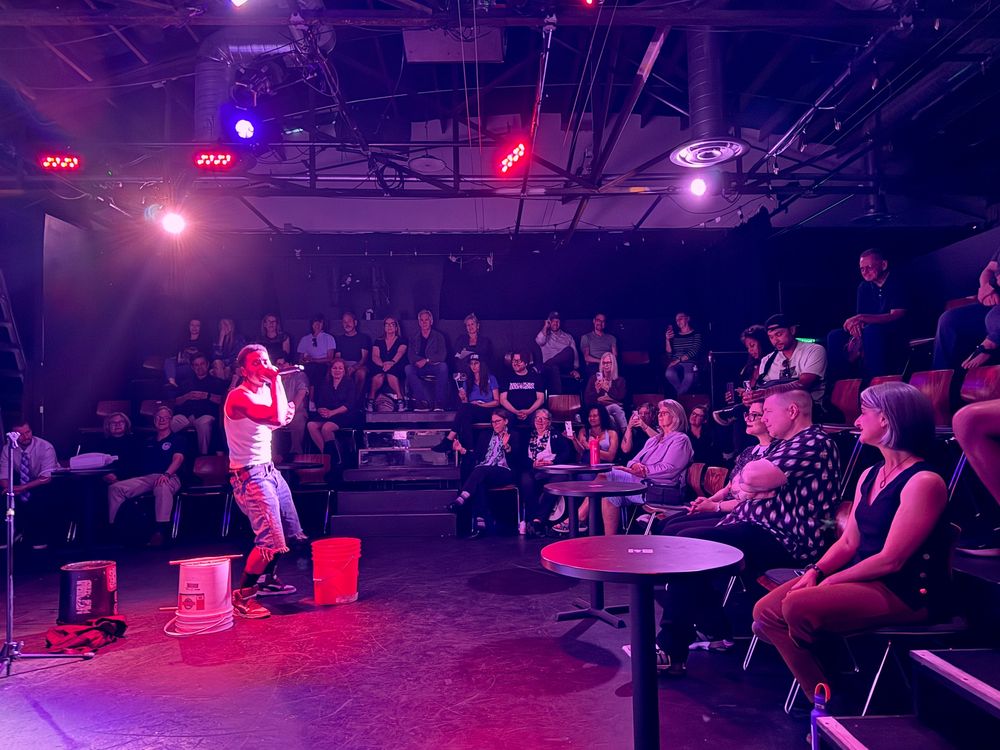 A performer is rapping into a microphone on stage with the audience looking on. 