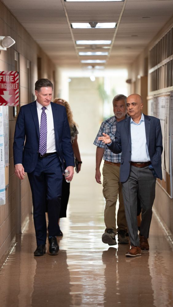 NSHE Chancellor McNair and DRI President Acharya walk with colleagues in a hallway, engaged in conversation. 