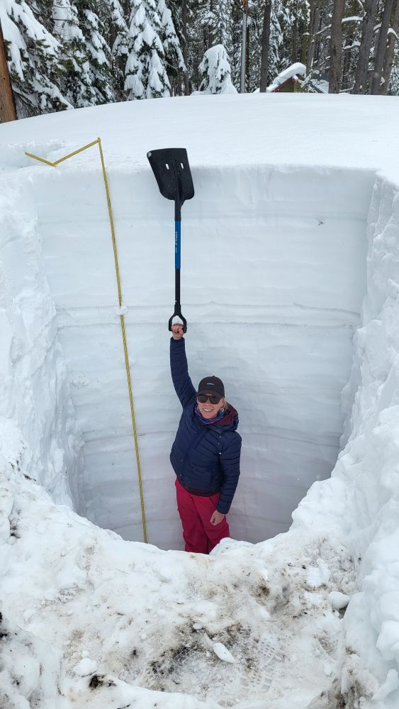 Researcher in snow pit holding a shovel to the top of the snow pit.