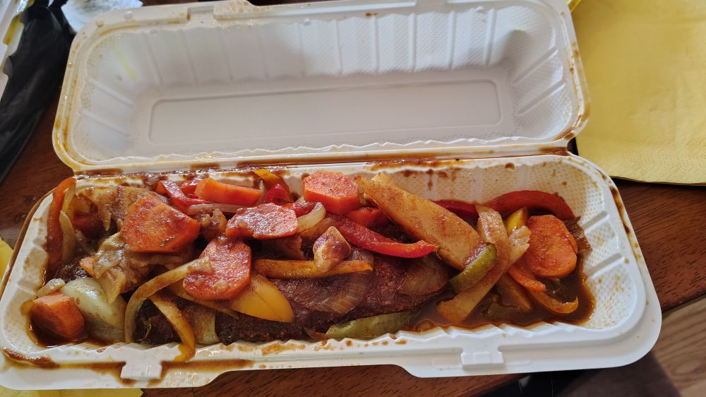 A takeout container with stewed brown snapper topped with vegetables 