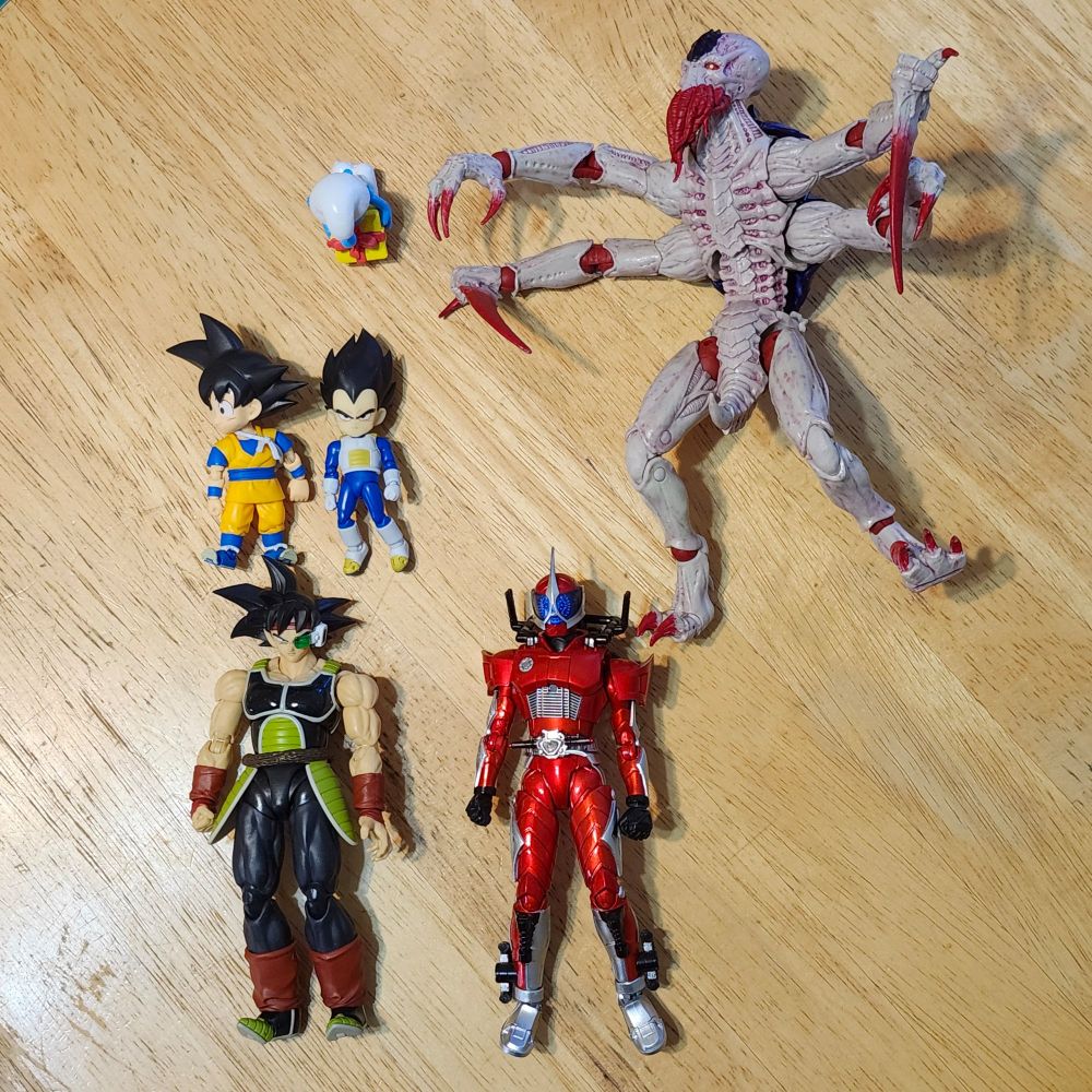 A bunch of toys laying on my table. 3 DBZ figures, a Kamen Rider Accel figure, and a McFarlane Tyranid