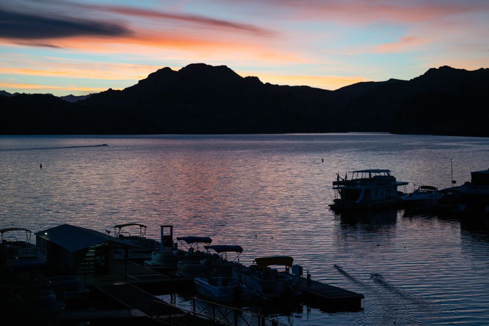 Sunrise at Saguaro Lake with two American coots landing and creating parallel wakes in the bottom right corner and a boat entering the top of the frame from the left.