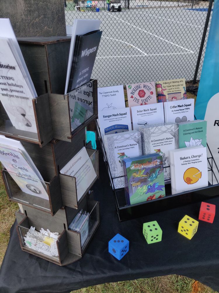 A photo of the contents of a TTRPG sales booth showing a variety of games in book, card, and brochure format