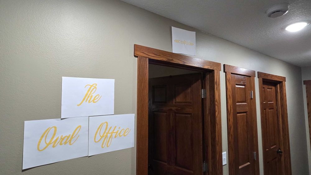 Crudely placed pieces of peasant printer paper with gold colored font that say The Oval Office.
