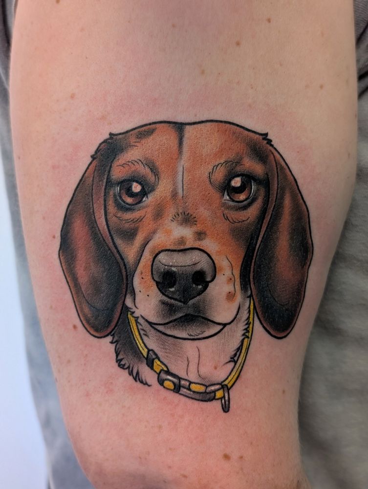 A tattoo on an arm of a beagle wearing a yellow collar.