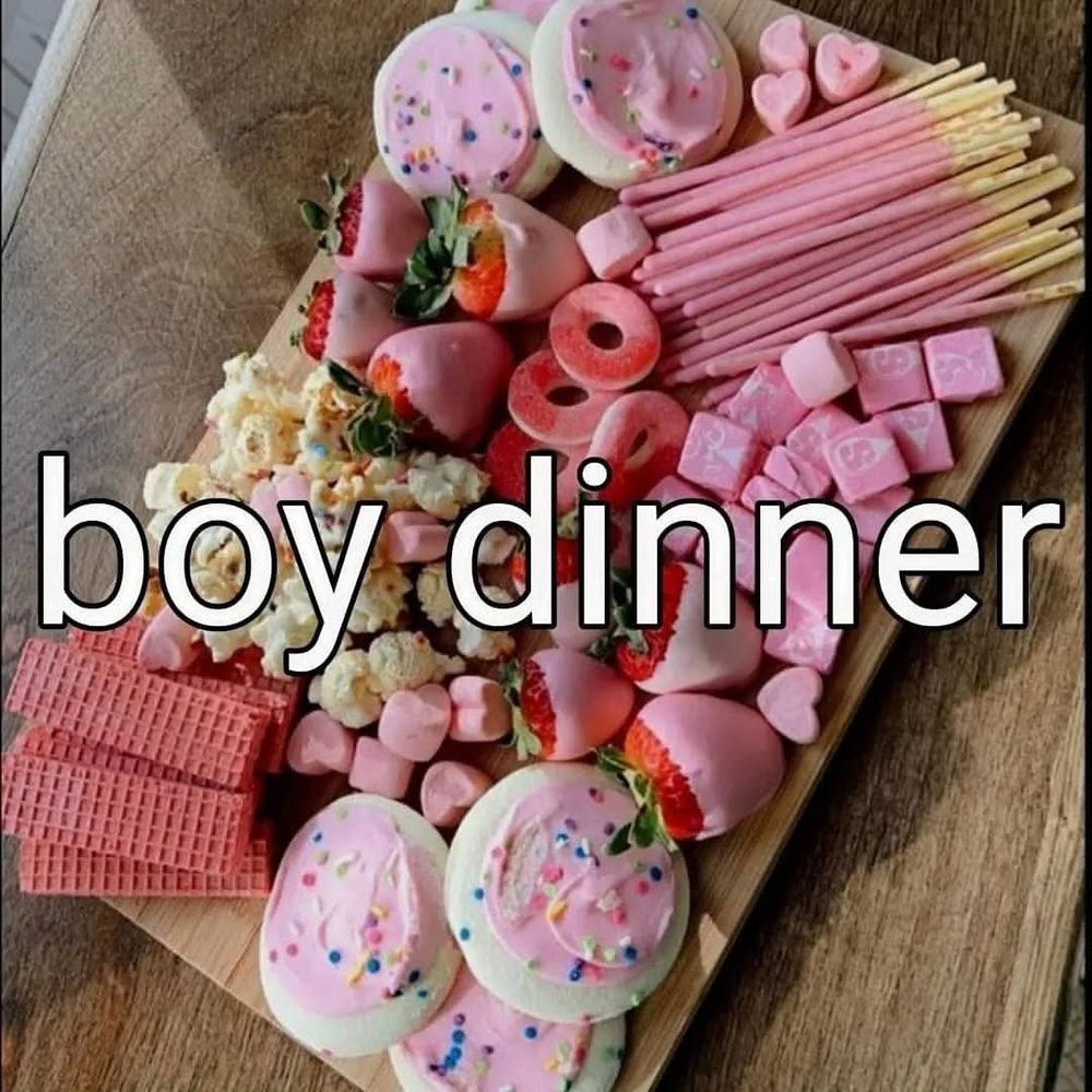 A charcuterie board with pink frosted cookies, pink wafer cookies, pink starburst, popcorn, pink peach rings, pink heart shaped marshmallows, and pink chocolate dipped strawberries. A caption says 