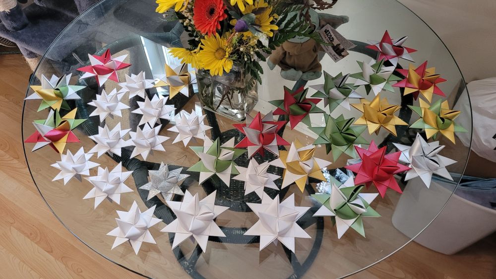 A table full of large and small German origami/paper-folded holiday stars, in assorted colors, also known as Froebel, Danish, Pennsylvania, advent stars.