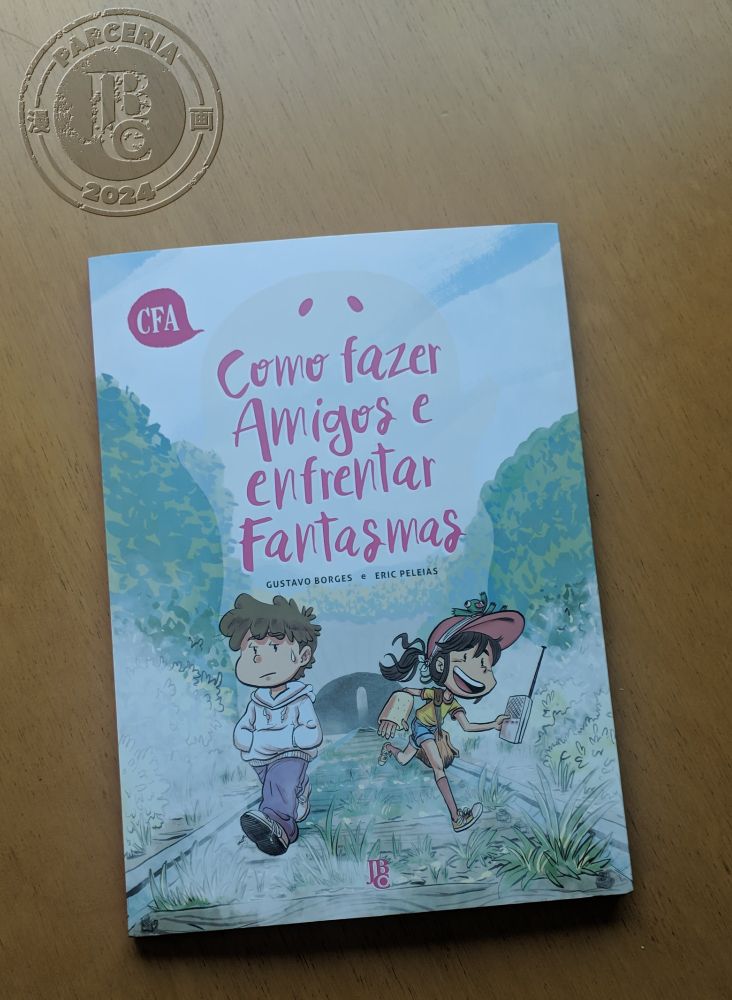 Capa do quadrinho Como Fazer Amigos e Enfrentar Fantasmas, de Gustavo Borges e Eric Peleias, em uma mesa de madeira. Acima dele, o simbolo de parceria JBC