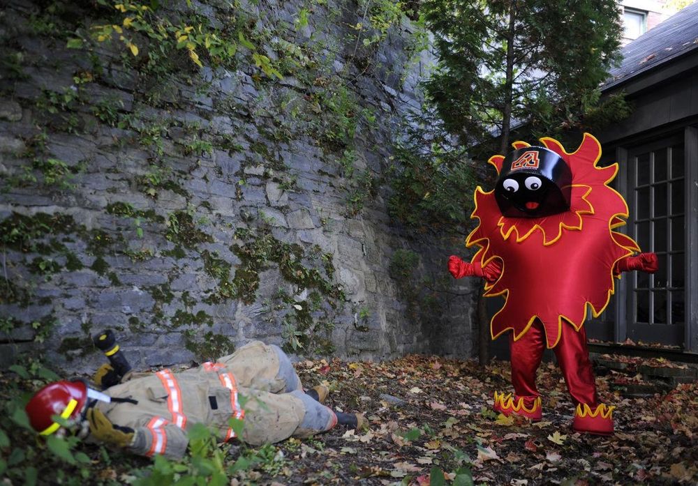 A mascot that is a flame with a hockey puck head standing over the body of a fireman 