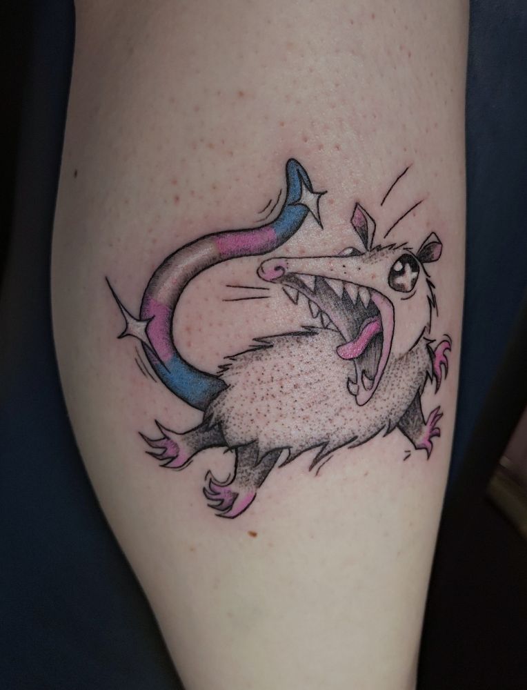 A tattoo on my calf. Its a possum leaping through the air, mouth wide in a scream. Its tail is colored like the trans flag. 