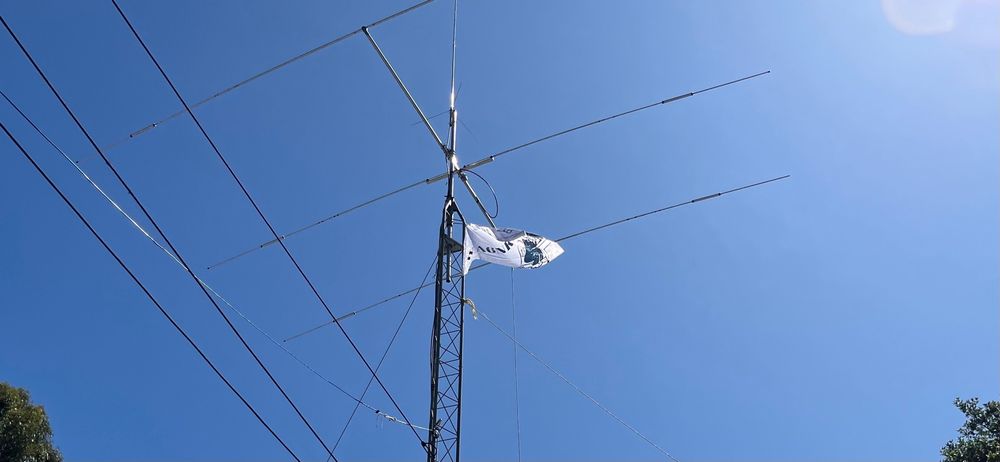 The white flag is attached to the tower just beneath the Yagi antenna at the top. Wires are running in the foreground towards another antenna. 
