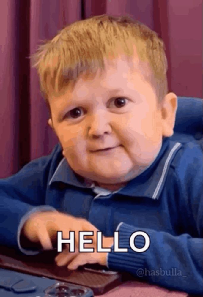 a little boy is sitting at a table with his hand on a keyboard and says hello