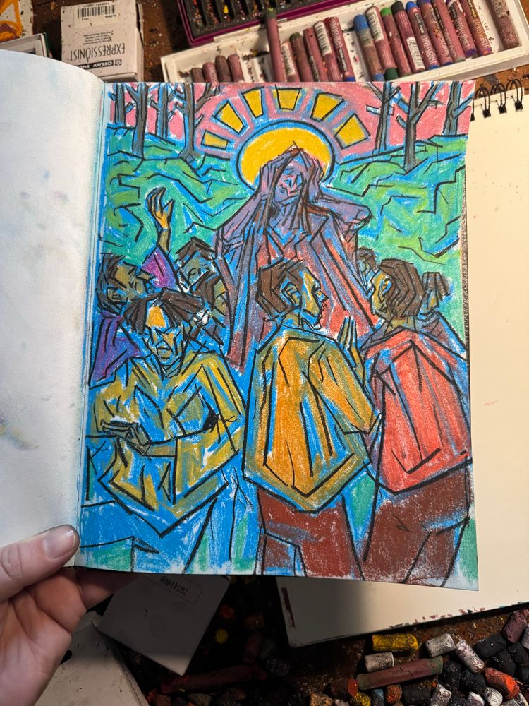 A hand holds and open hardbound sketchbook over a messy and materials-strewn artist’s table. Inside the book is a conte crayon drawing of a crowd of people mobbed around an awakening saint. Art by Jason Thomas Pitzl. 
