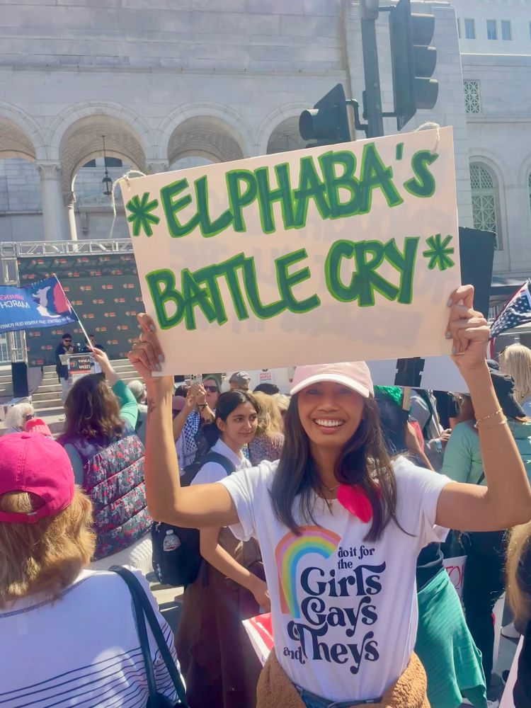 Woman holding a sign that reads “Elphaba’s battle cry”