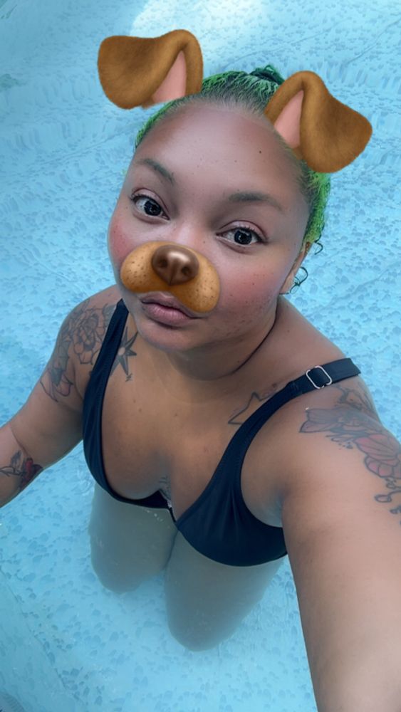 Sitting in a backyard pool with a black bikini. Wearing the Snapchat puppy filter with big eyes 