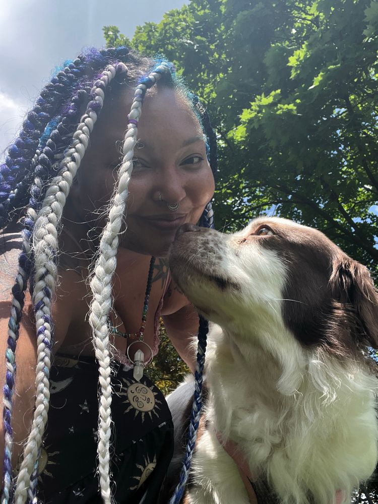 Leaning down smiling, my brown and white border collie mix looking up at me. Trees behinds us. 
