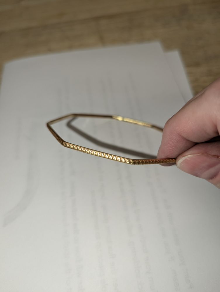 A brass octogon-shaped brass bracelet with a rope-like pattern imprinted on the metal.