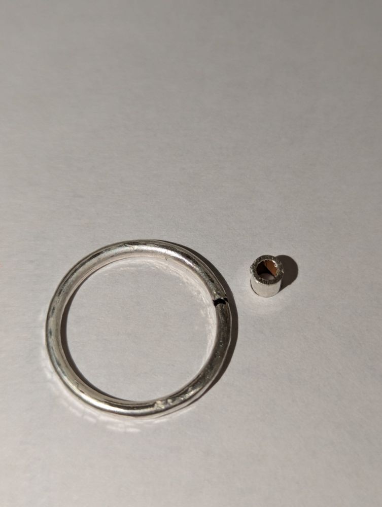 A silver ring with a black sharpie mark indicating where I'm going to cut it & remove a piece. Next to the ring is a small silver tube.