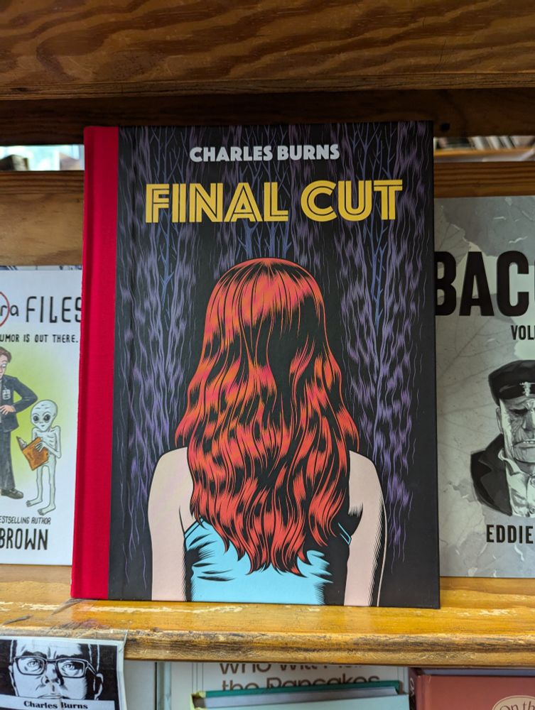 The cover for Charles Burns' graphic novel FINAL CUT has a red binding. We can see the back of a white person with long red hair, wearing what looks like a blue tank top. The background is some sort of organic purple pattern, similar to woodgrain.