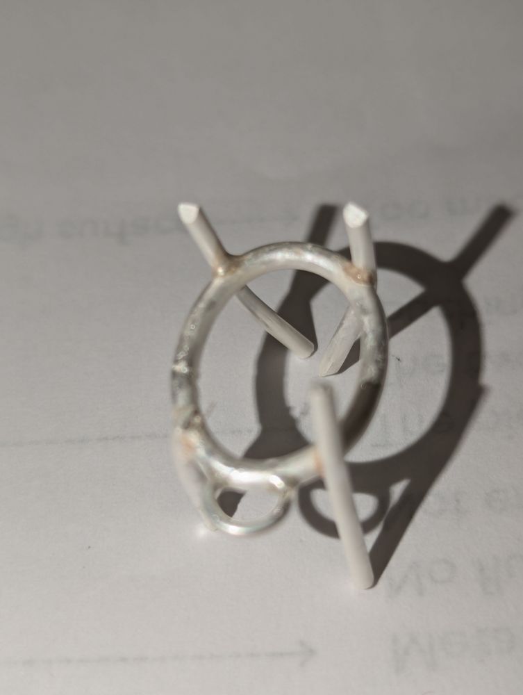 Oval silver wire with a small loop on one end and four pieces of wire soldered in place perpendicular to the oval at the four "corners." Extremely janky looking.