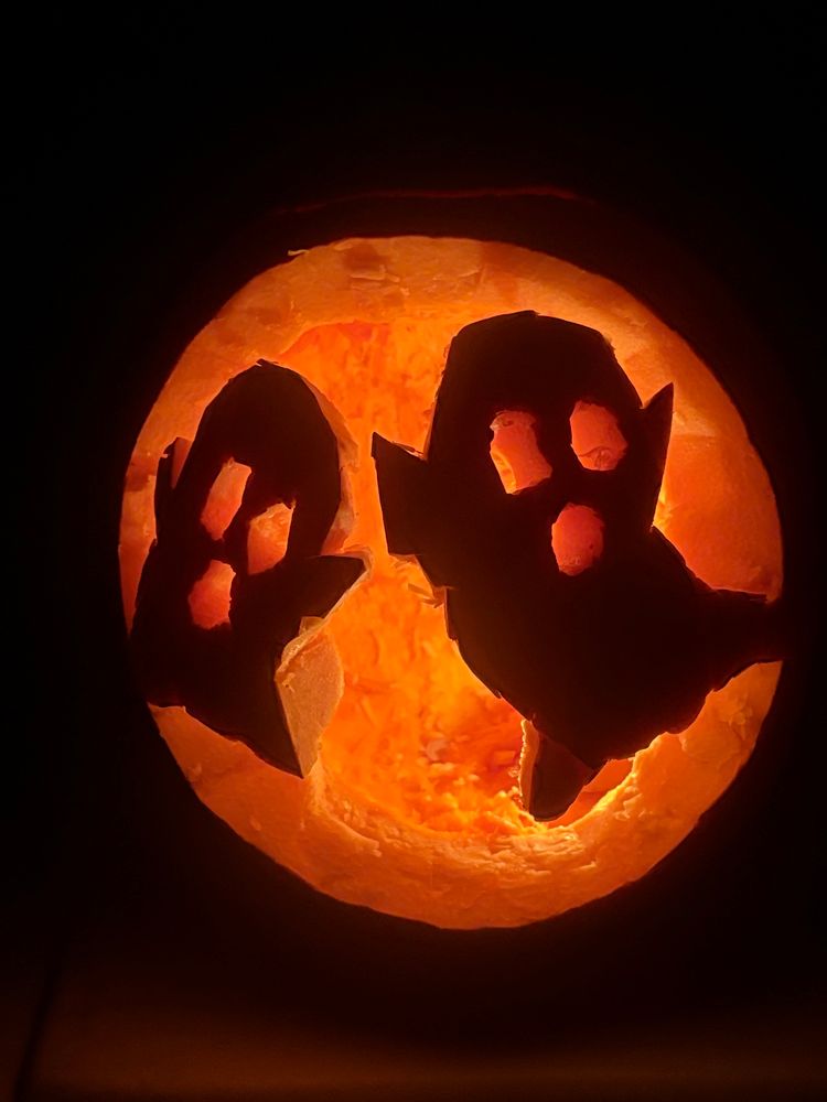 A lighted pumpkin carved with two kind of janky ghosts 
