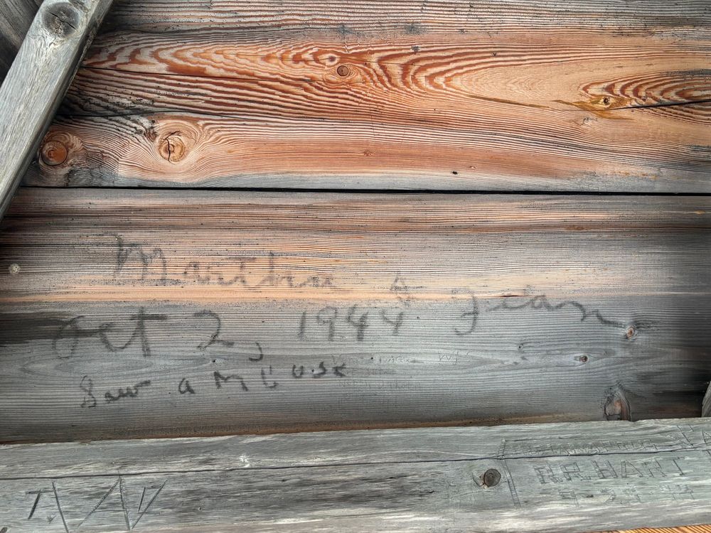 Cursive black writing on a worn wooden board reading “Martha & Jean, Oct 2, 1944 Saw a Moose”