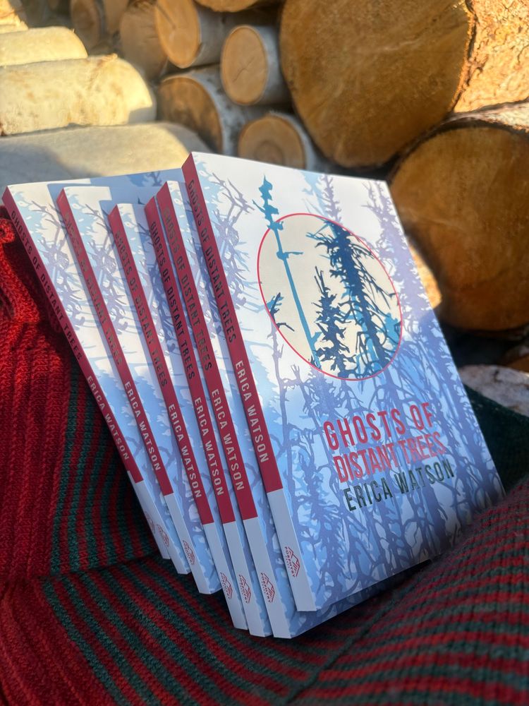 A stack of 7 copies of Ghosts of Distant Trees half lit by sunlight, propped up in a wood pile, sitting on a red and teal knit shawl 
