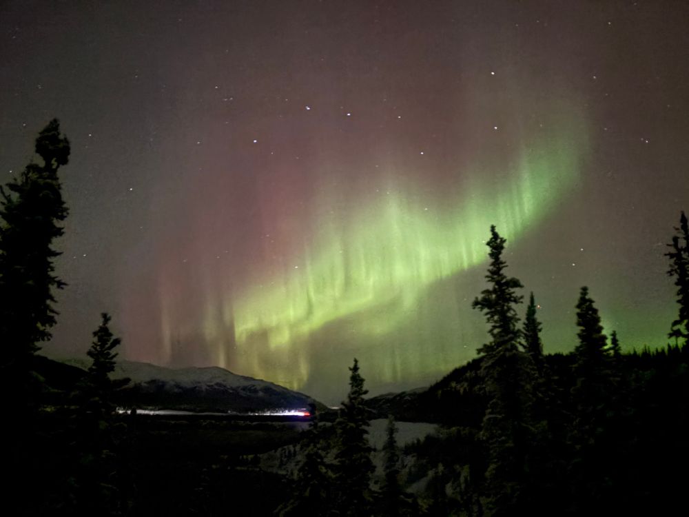 A green curtain of aurora, with highway traffic visible in the lower 3rd, and the Big Dipper constellation in the sky 