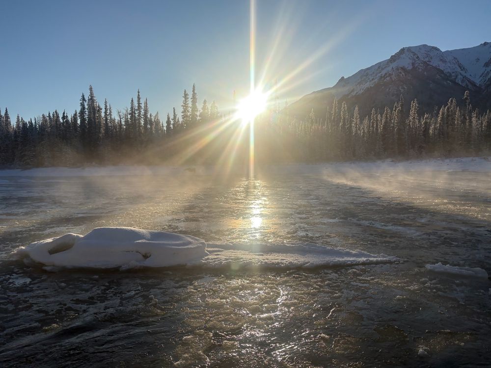The sun descends across a river, with ice starting to form but still plenty of open water. It’s steaming a bit in cold air. 