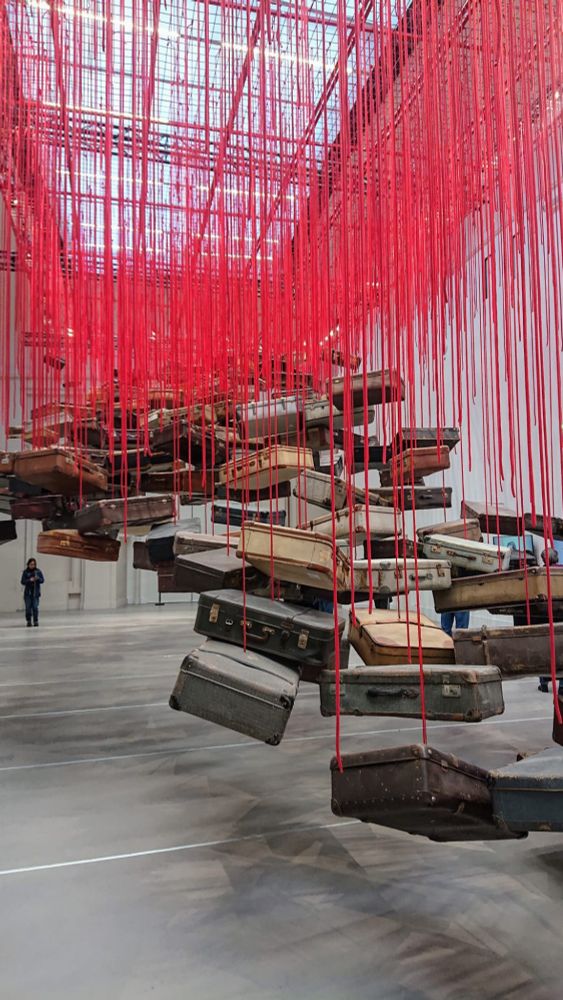 Chiharu Shiota art installation that has many old fashioned luggages suspended in air, stranding from the ceiling by thick red ropes.