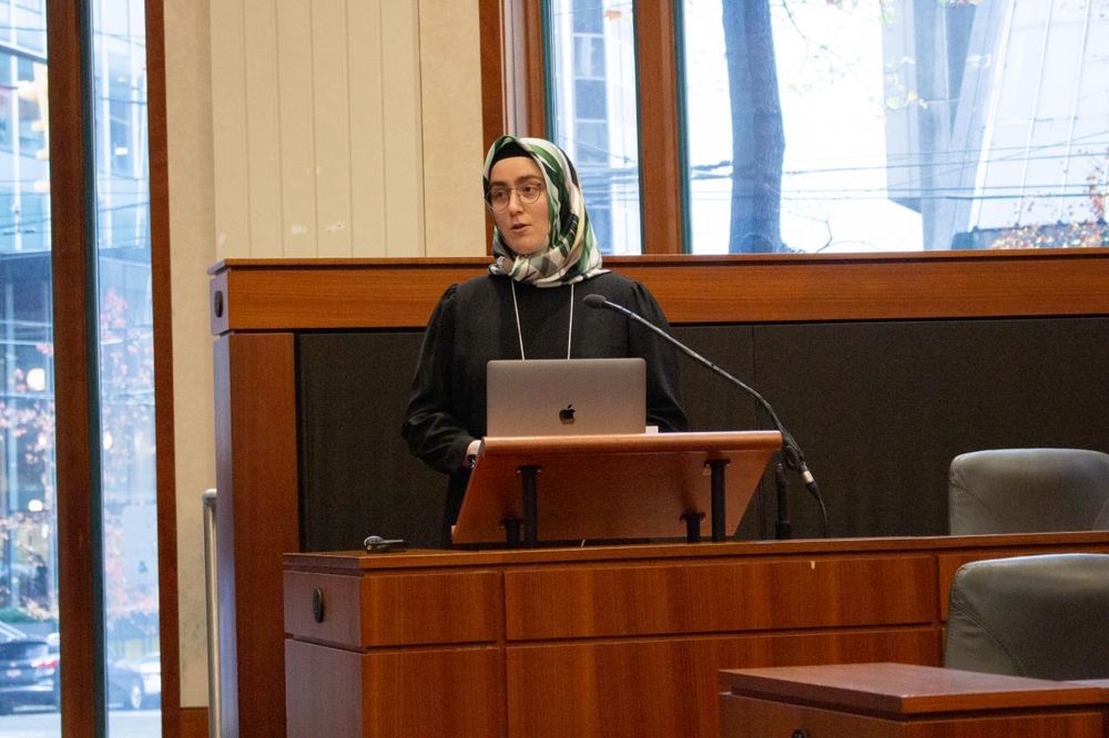 Sena Kholmatov speaks at a wood-paneled lectern with a laptop and mic during SFU’s Research Day on Aging.
