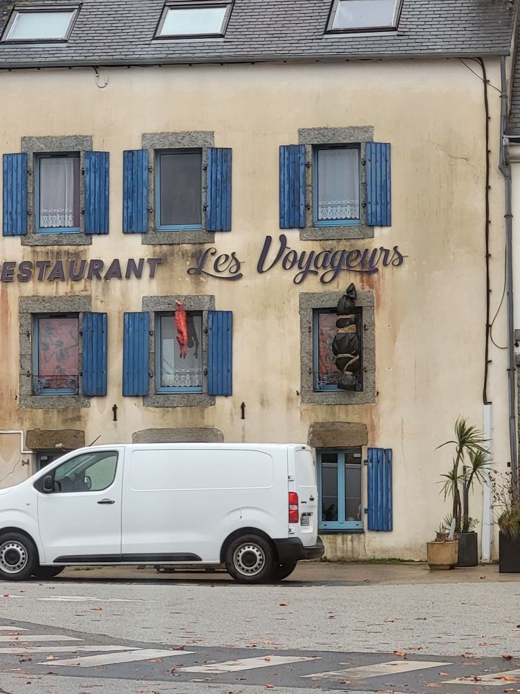 French restaurant with what appears to be a plastic wrapped body hanging outside.