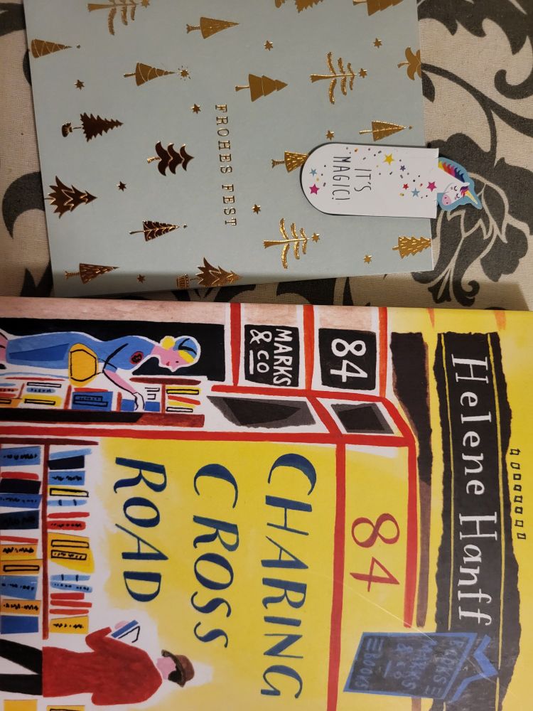 Eine Karte mit goldenen grafischen Weihnachtsbäumen. Ein Einhornlesezeichen mit dem Text "It's magic". Die Titelseite des Buchs "84 Charing Cross Road" von Helene Hanff