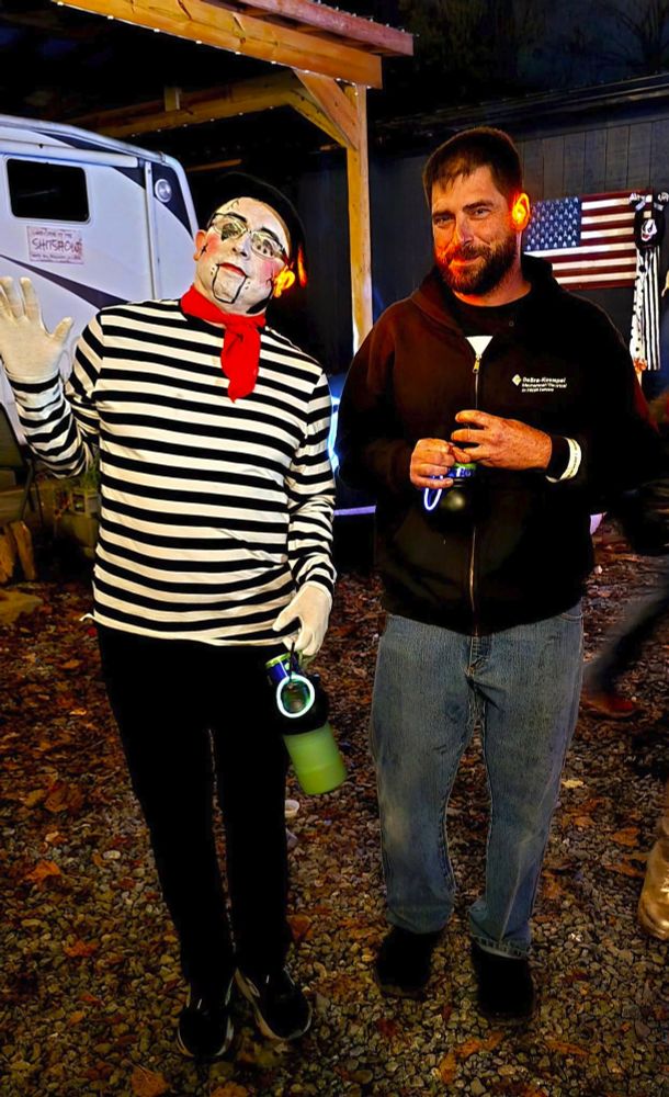 OP in a French Mime-as-marionette outfit, with striped shirt, red neckerchief, and facepaint emphasizing porcelain cracks and a moving jaw waving to the camera next to a taller dark haired man. 