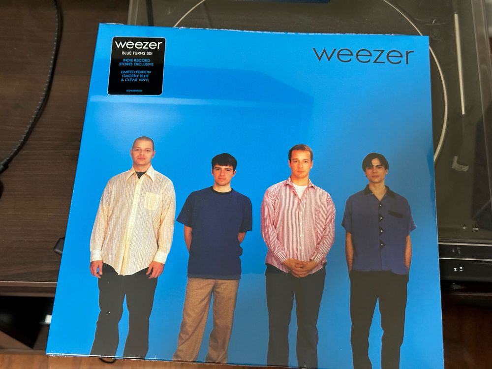 A picture of a vinyl record of weezer. It is all blue with black small lettering labeled weezer. Four men stand on the cover. 