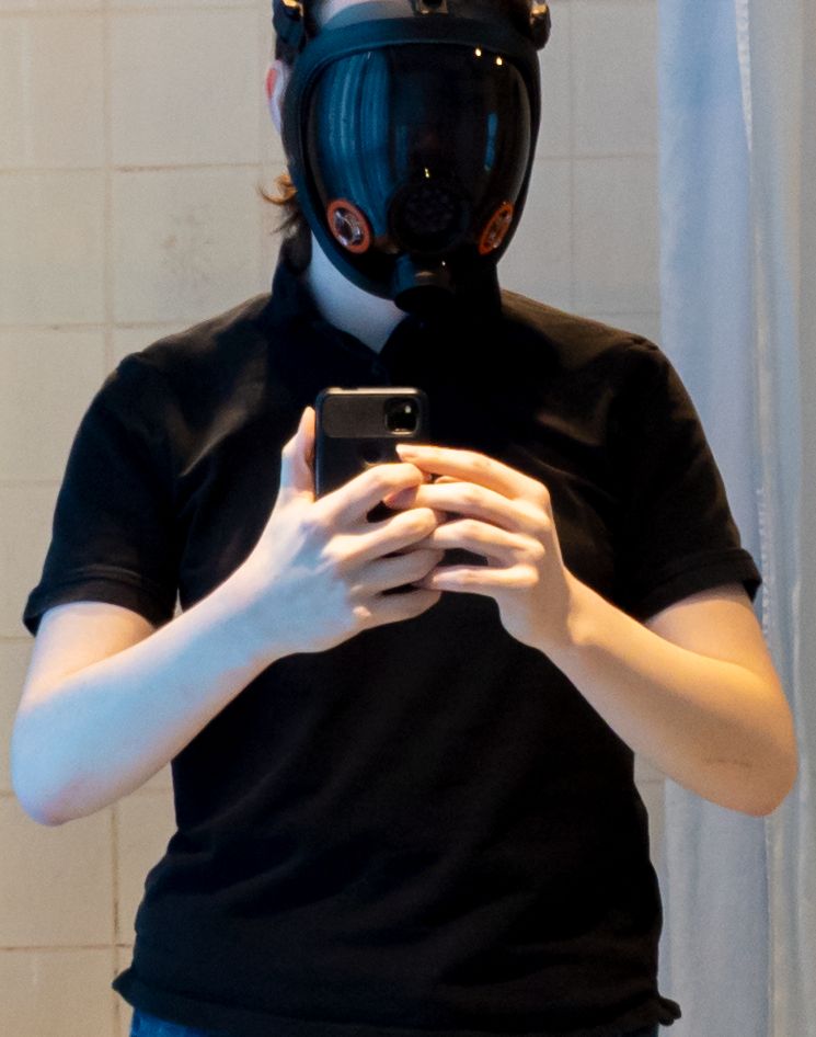 A drone wearing a Parcil PD-100 mask and a black t-shirt, facing the viewer with arms at chest level
